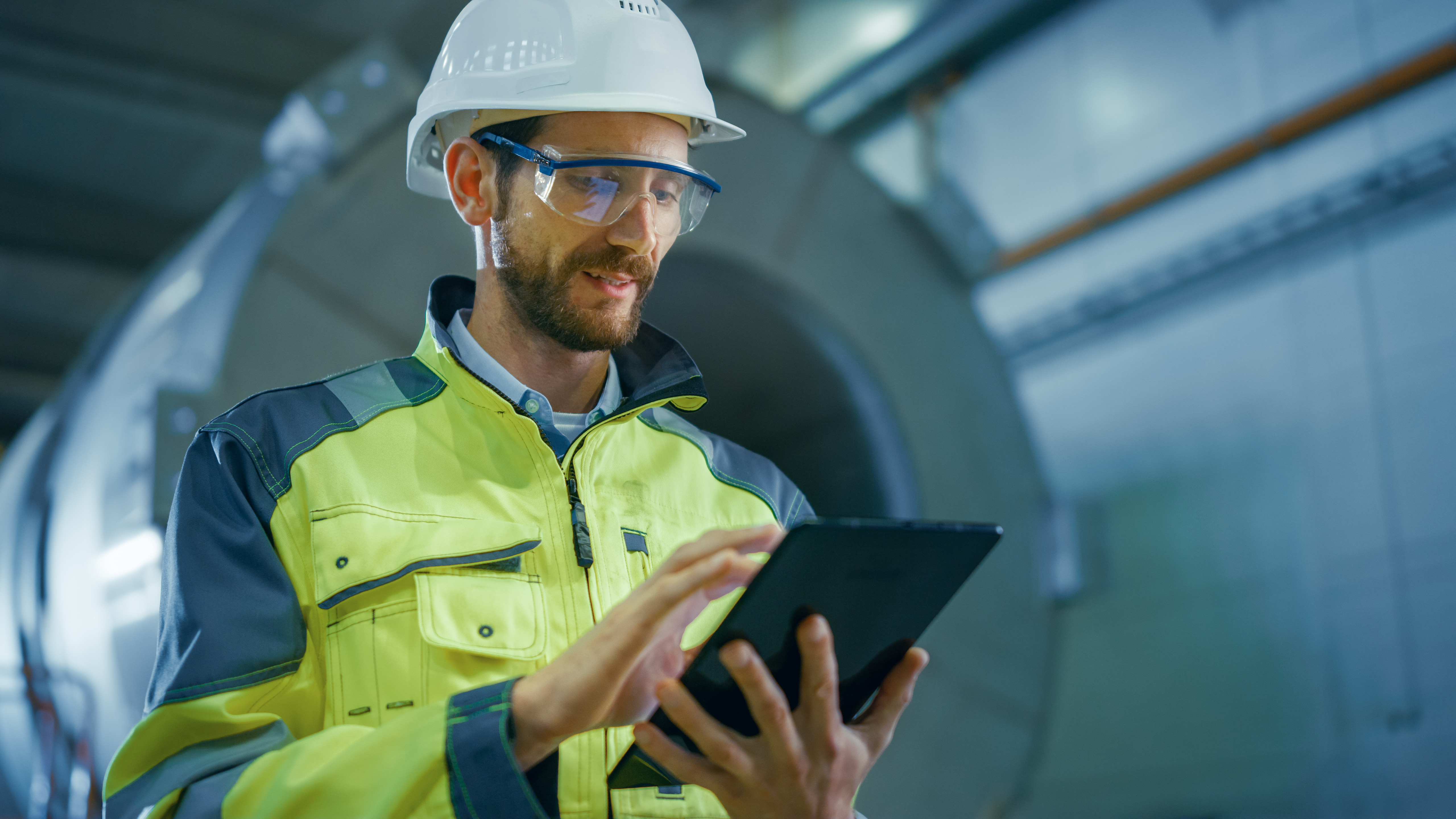 Engineer in protective gear reviewing operational data on a tablet inside an industrial facility, symbolising third-party verification and assurance for corporate greenhouse gas reporting