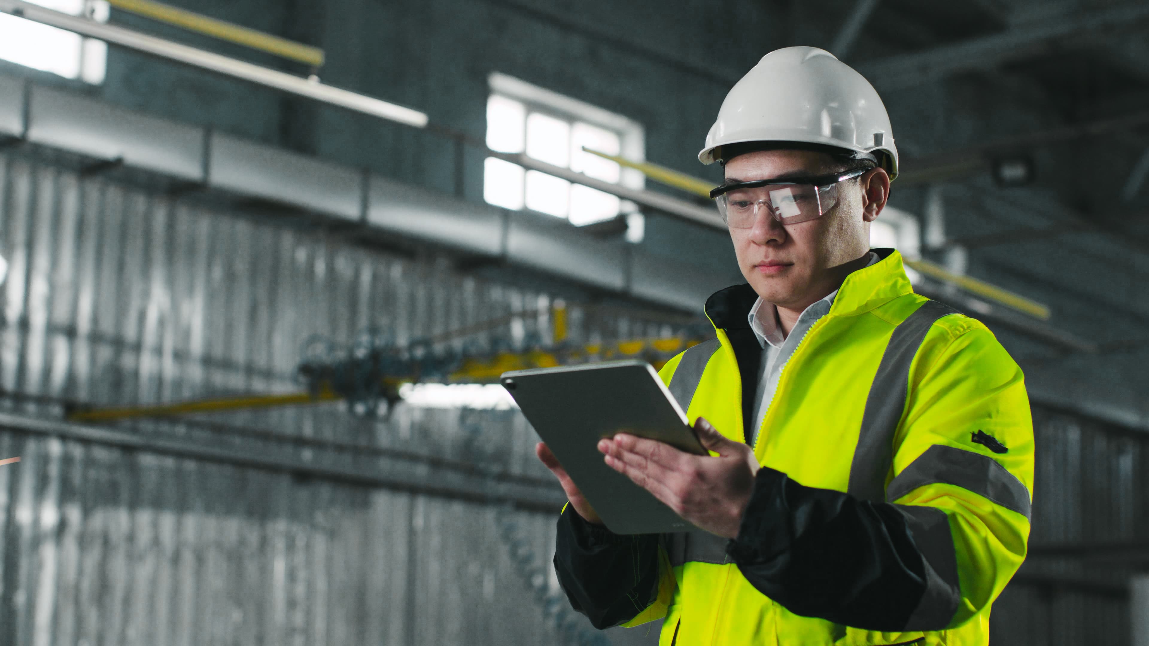 worker looks a tablet, wearing high vis and hard hat
