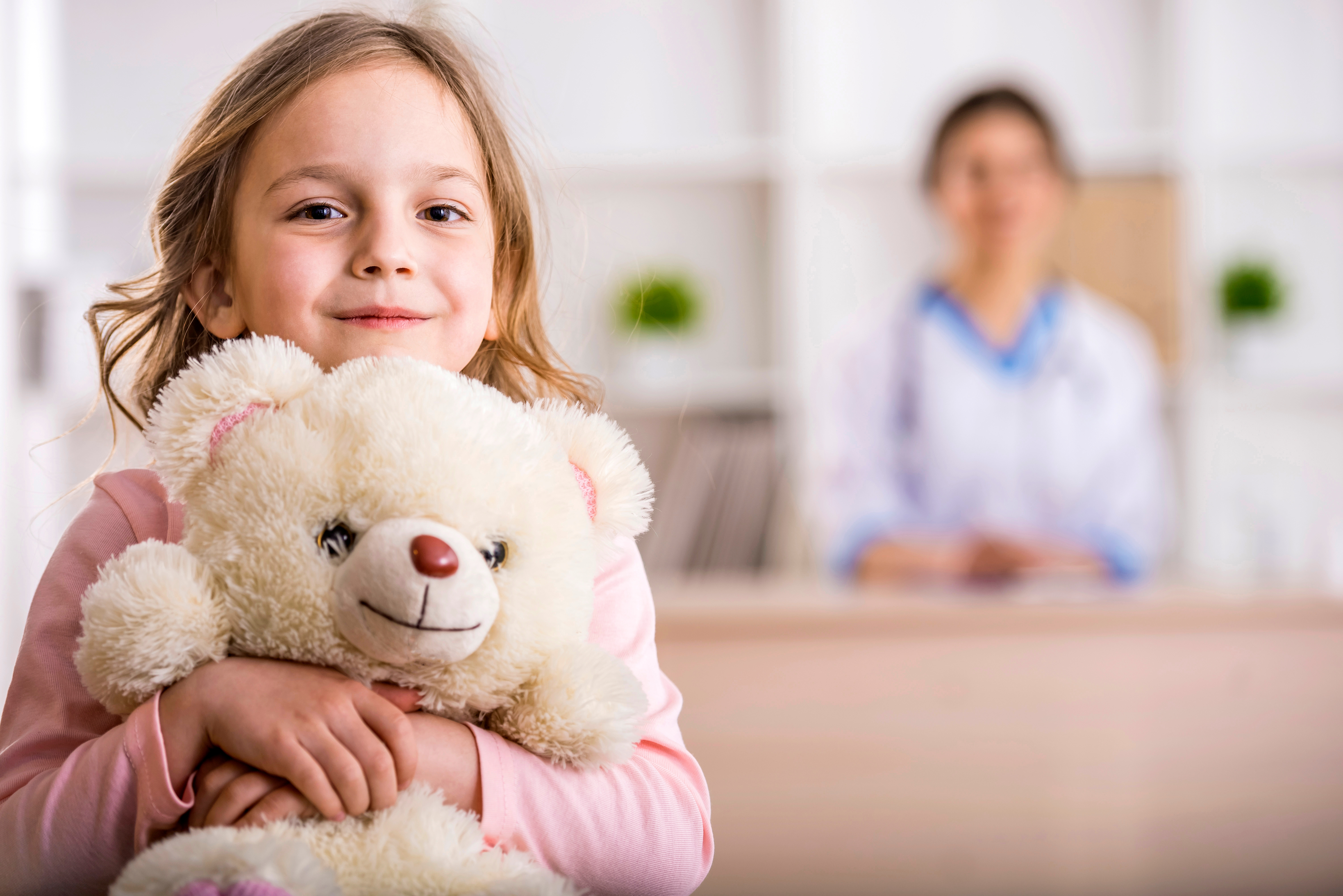 Smiling child holding a teddy bear in a clinical setting, reflecting high-quality, compassionate care in paediatric spine programs