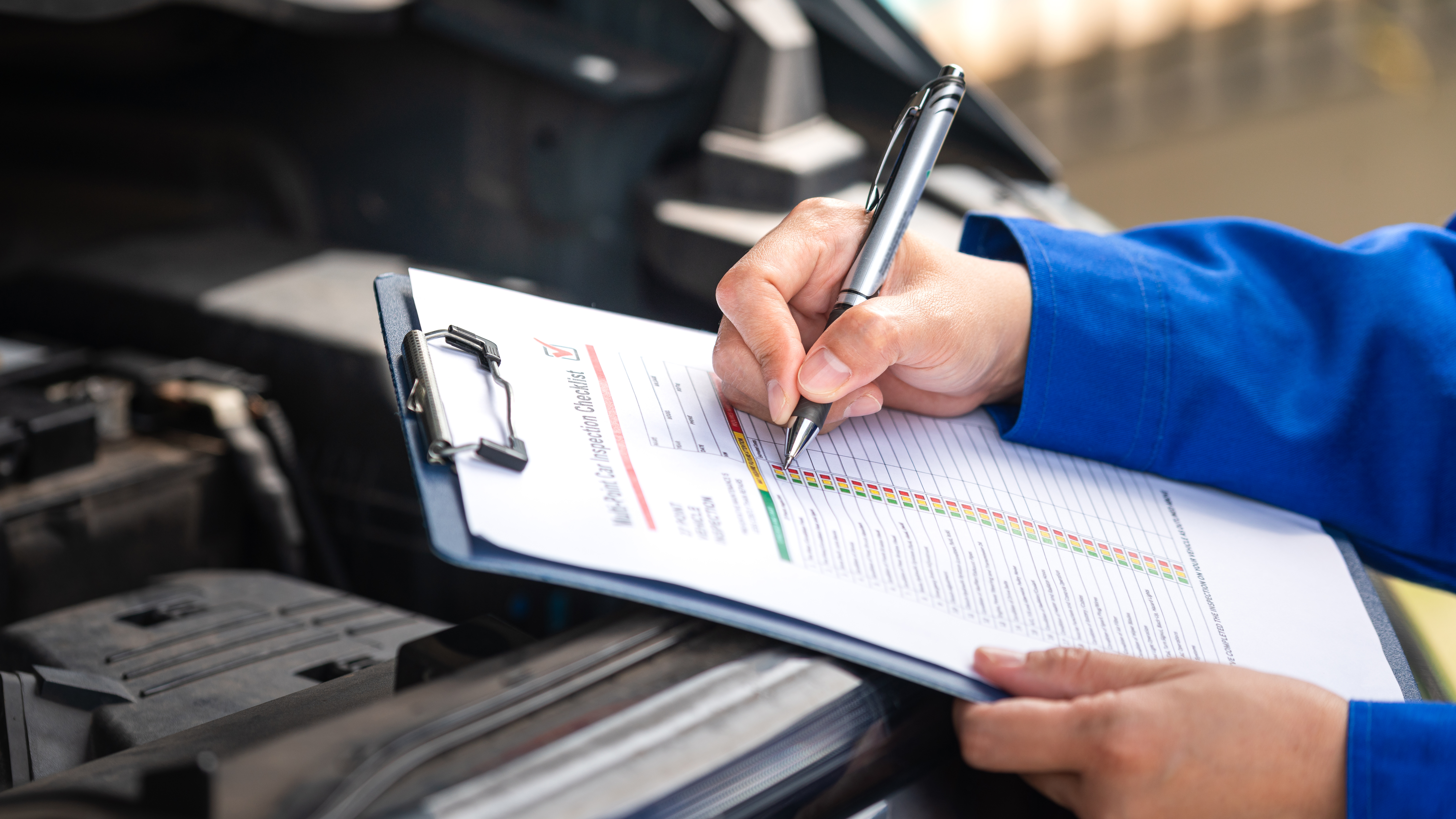Engineer documenting failure analysis findings on a checklist while inspecting a vehicle engine