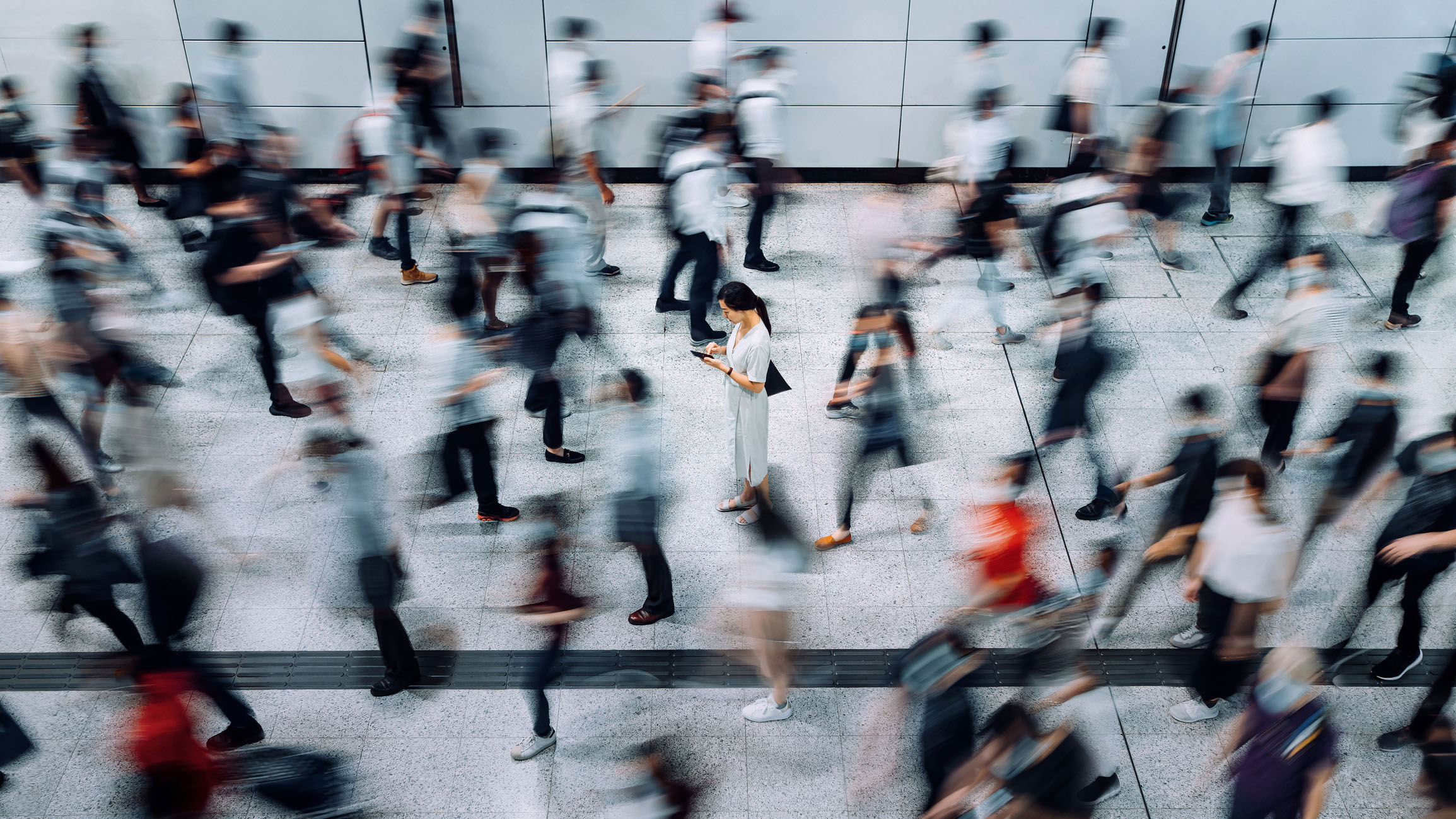 Young woman using smartphone surrounded by commuters rushing by
