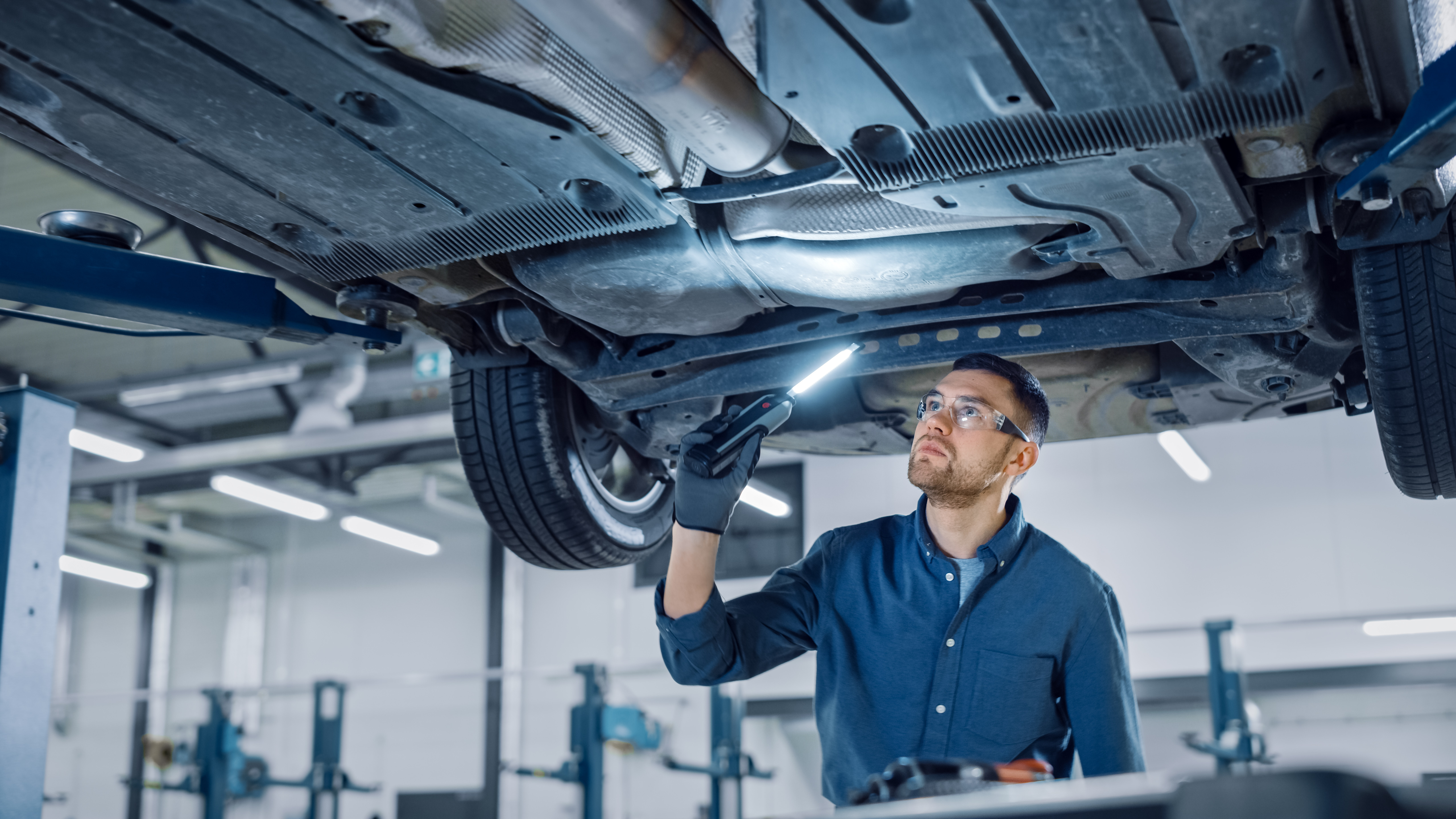 Automotive engineer inspecting a vehicle on a lift to assess mechanical and electronic components for cybersecurity vulnerabilities