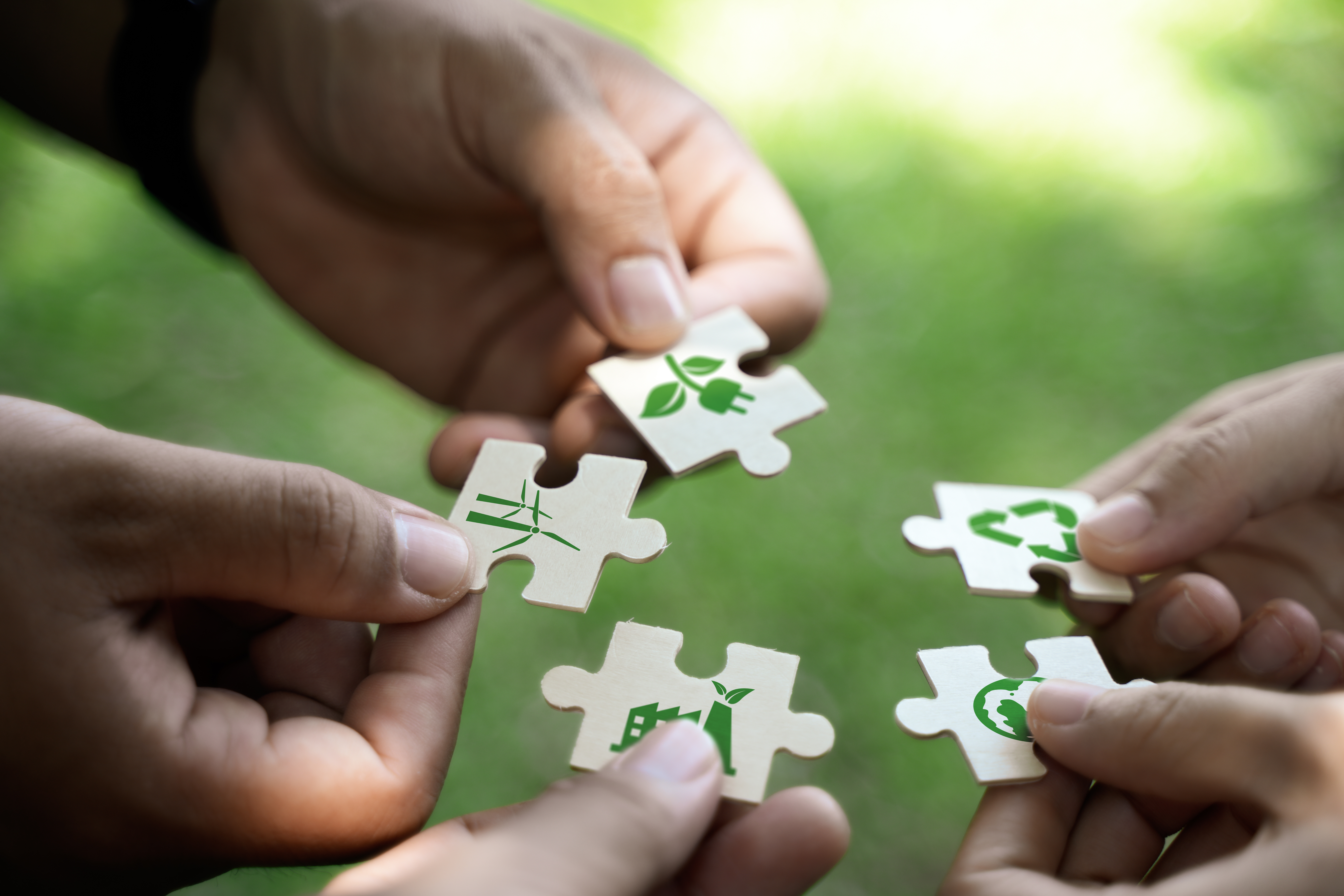 Hands assembling green sustainability-themed puzzle pieces, symbolising collaboration in building an effective net-zero strategy
