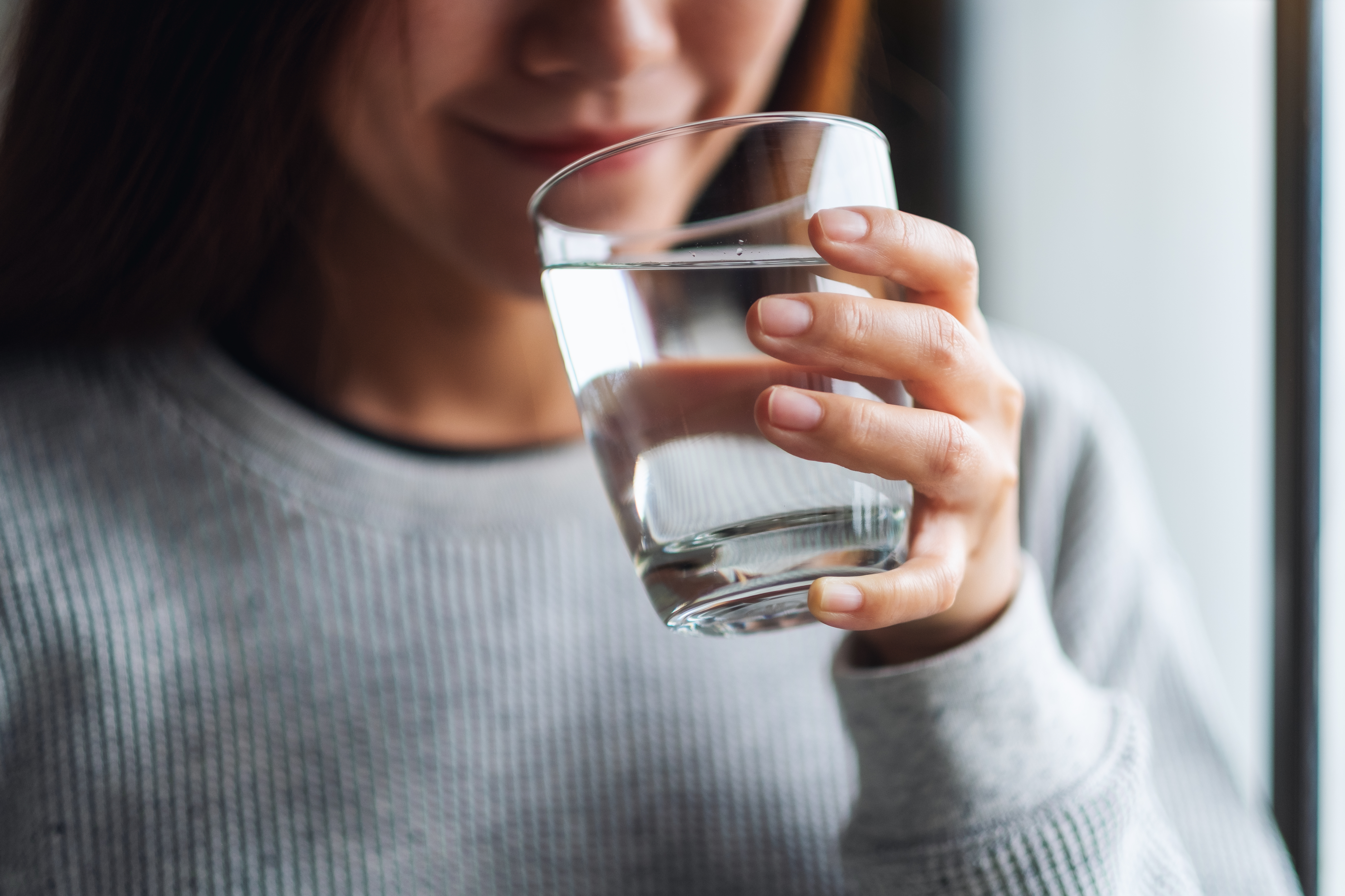 Woman drinking a glass of clean water, symbolizing trust in food safety, hygiene, and quality verification.