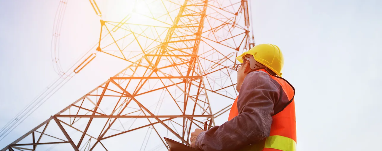 Worker standing at transmission tower - electric grid