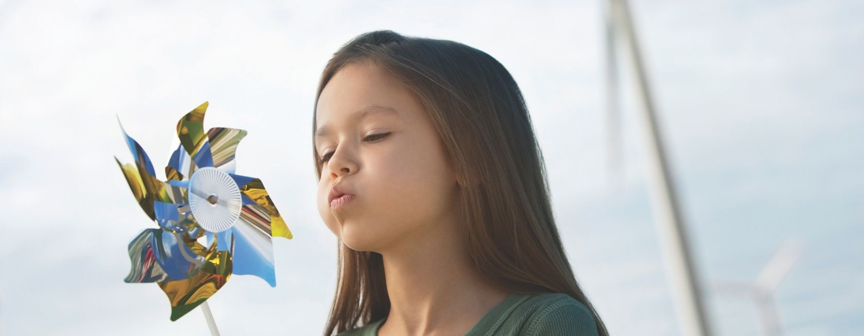 Girl blowing toy windmill at wind farm