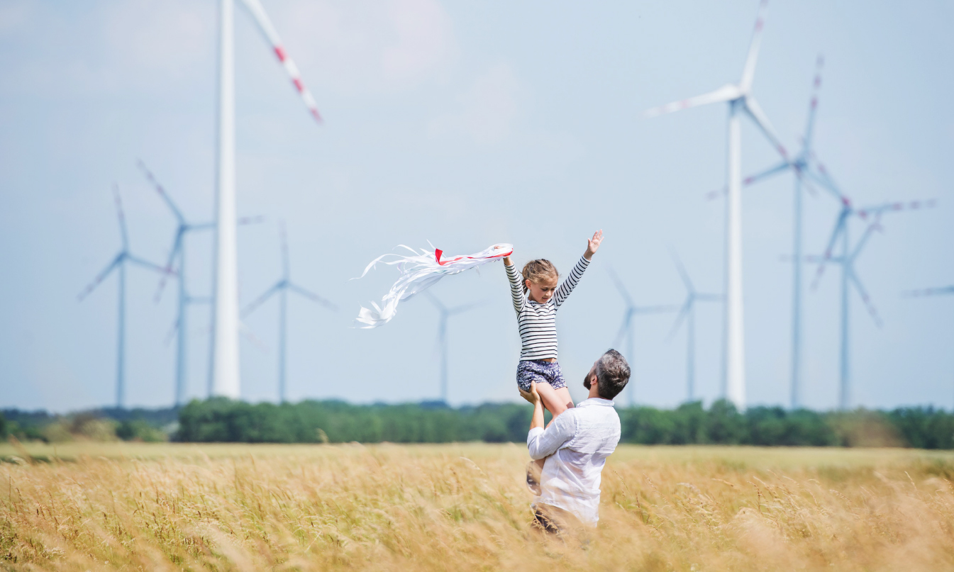 People on a field with wind turbines in the background