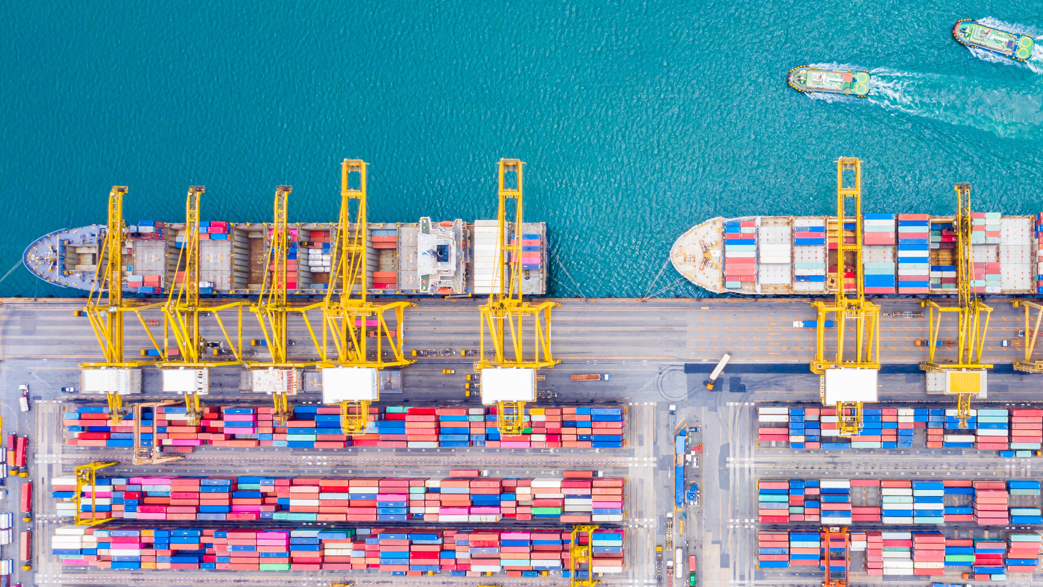 Aerial view of container ships docked at a port with colorful shipping containers and yellow cranes