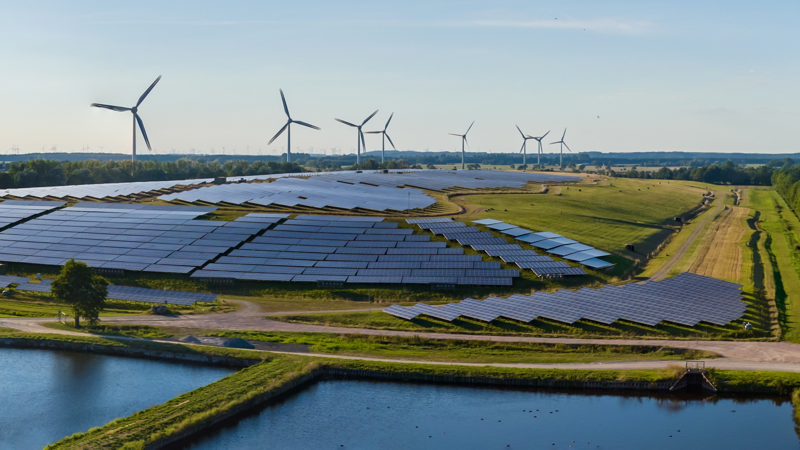 Aerial view of sustainable energy facilities with wind turbines and solar panels near water, symbolizing climate-aligned finance and renewable transition projects.