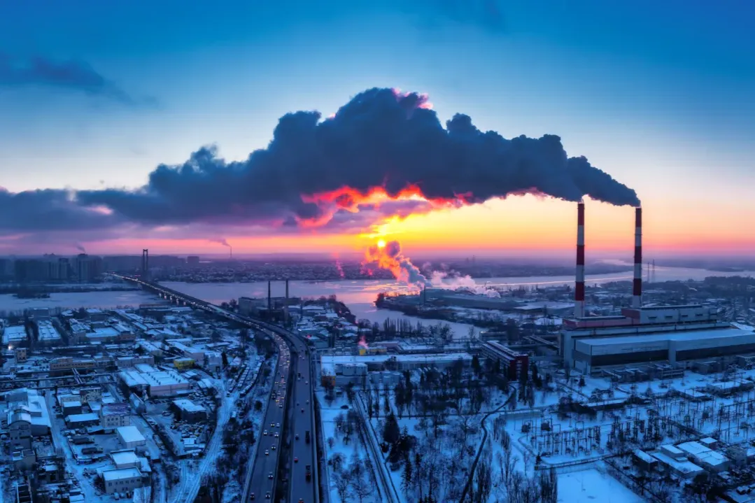 Industrial facility emitting smoke under a sunset sky