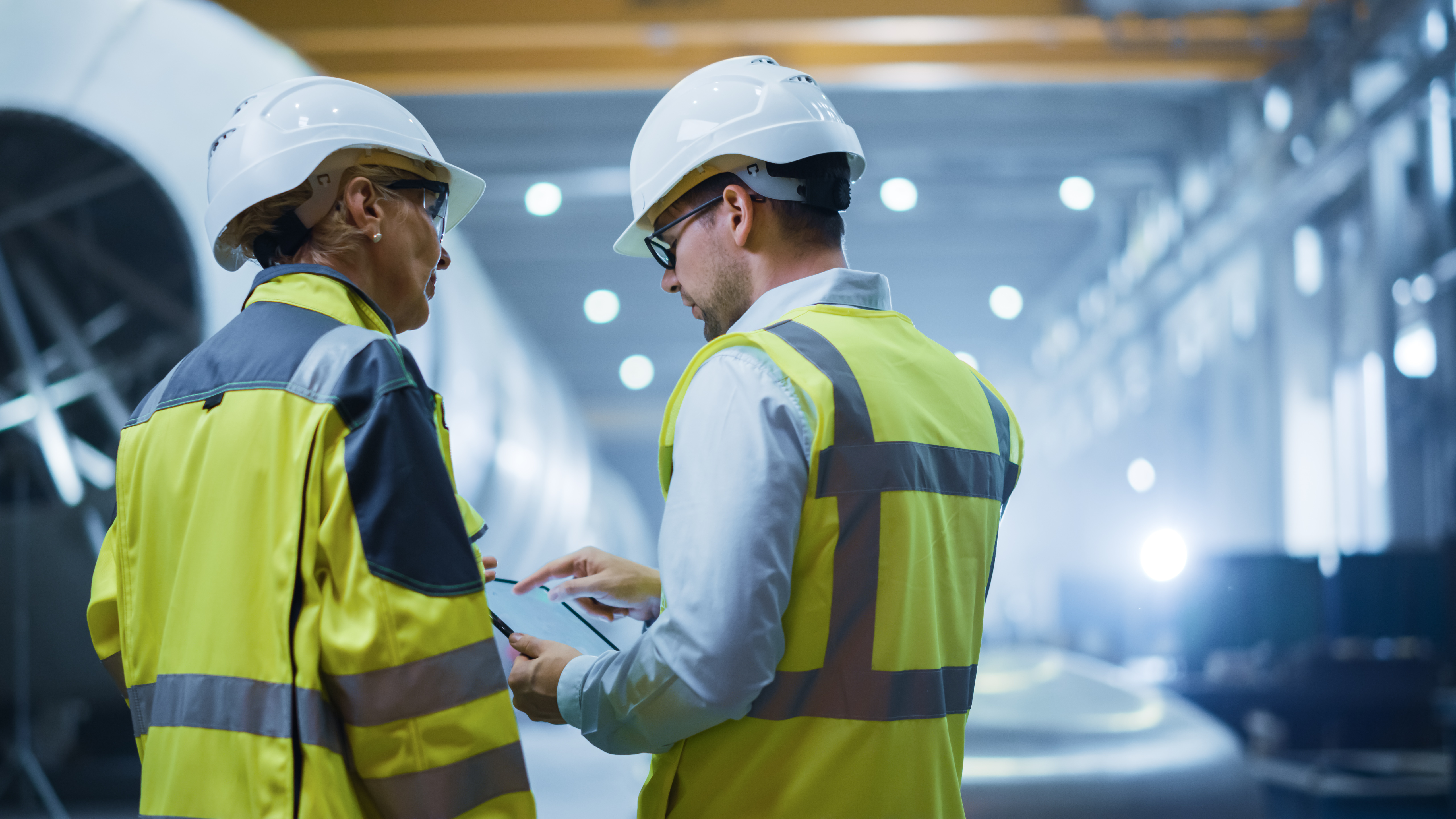 Two engineers in safety gear inspecting material flows inside a heavy-industry facility