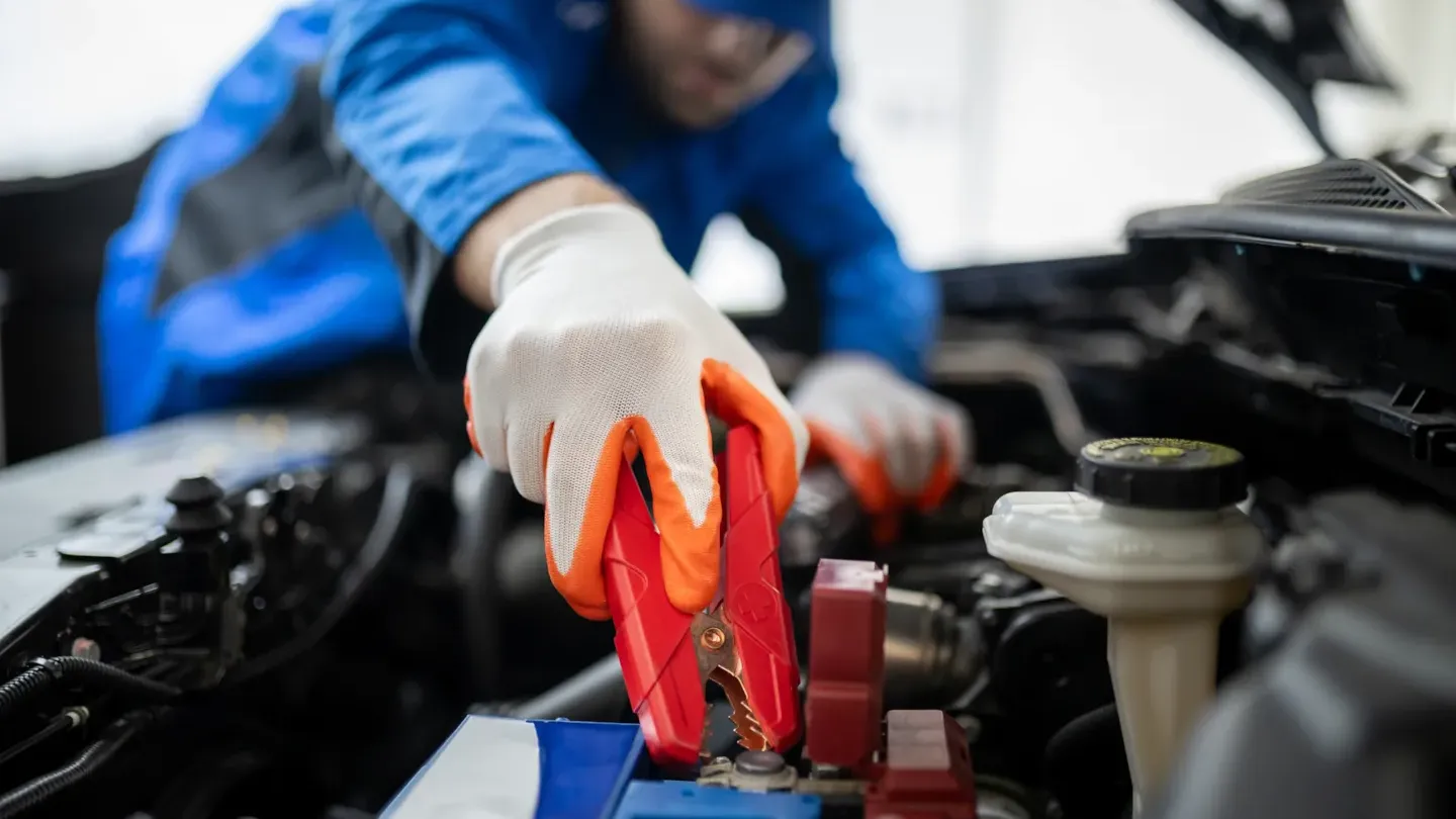 Automotive technician attaching diagnostic jumper cables to a vehicle, representing reliability testing and performance evaluation
