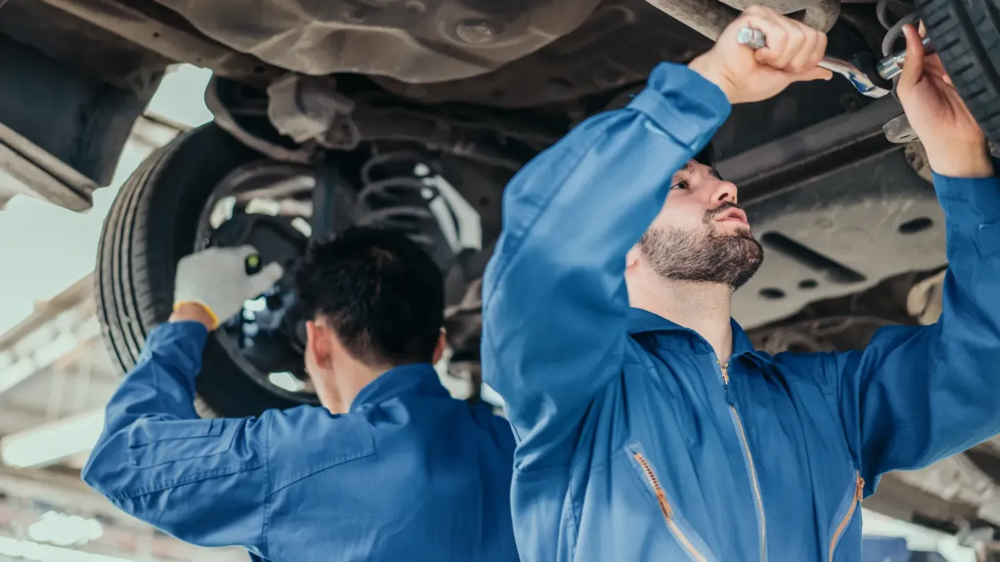 Engineers receiving hands-on functional safety training under a vehicle, demonstrating practical ISO 26262 competency development