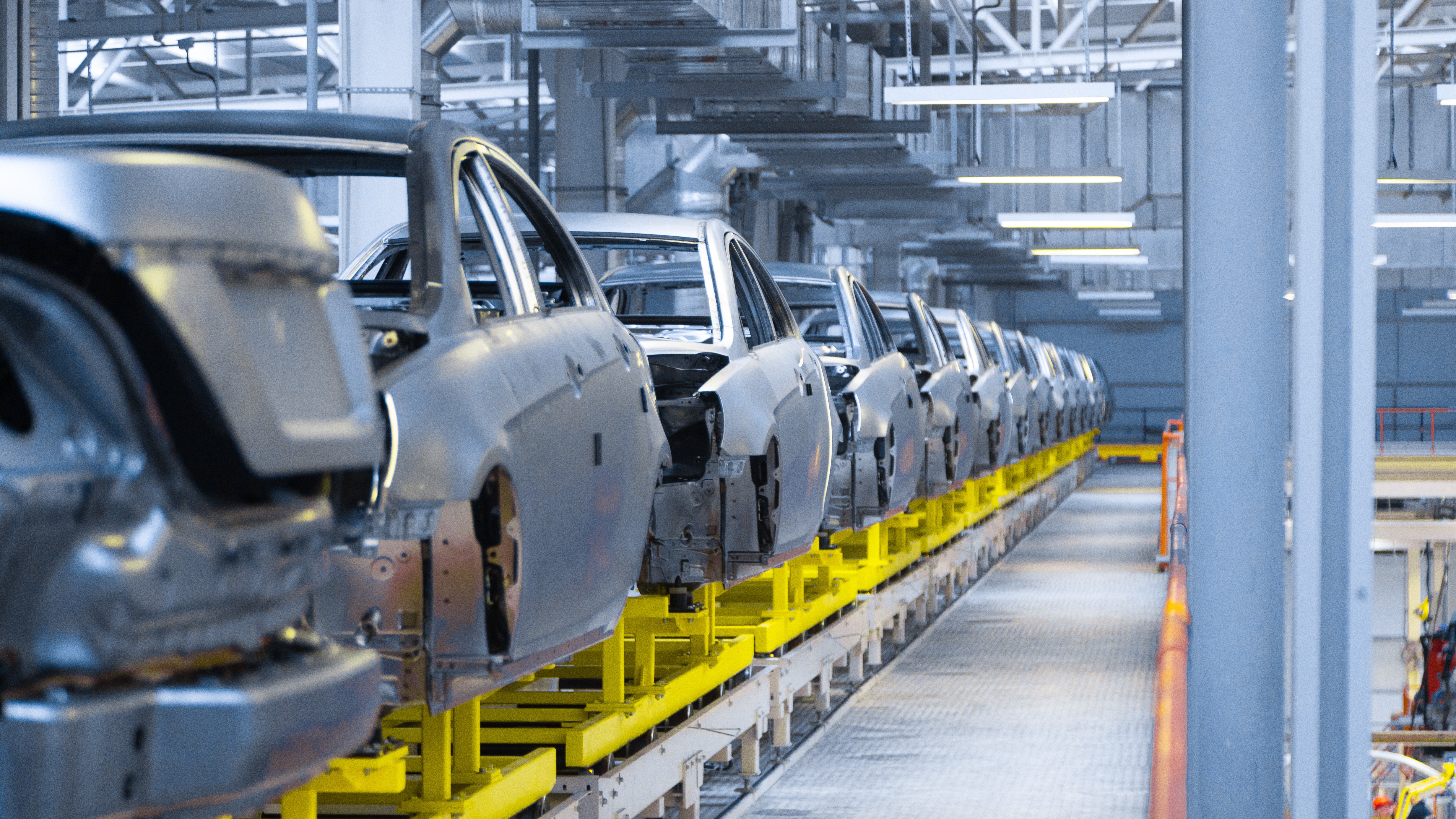 Overhead view of partially assembled car bodies on an automotive production line, illustrating development and compliance checks in manufacturing