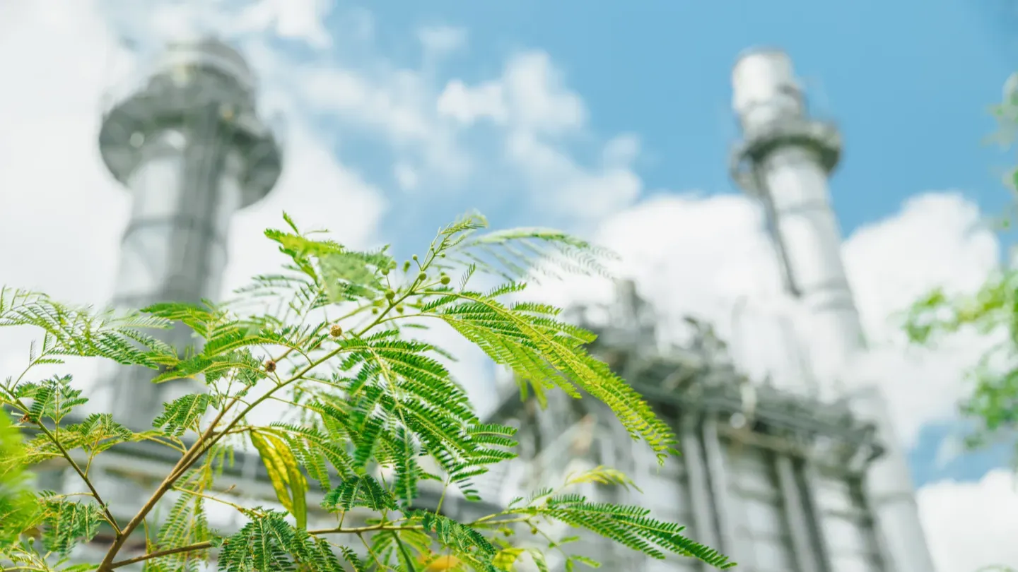 Industrial facility with emissions stacks surrounded by greenery, representing material traceability and verified sustainability claims across complex value chains