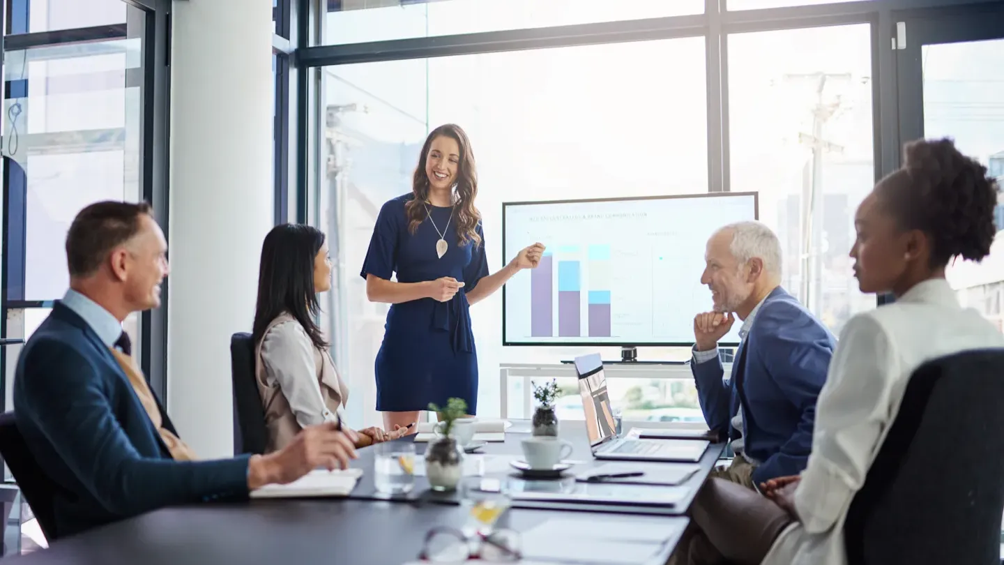 Business professionals collaborating in a meeting room with sustainability charts visible on a screen, representing DNV’s climate, biodiversity, and decarbonization expertise