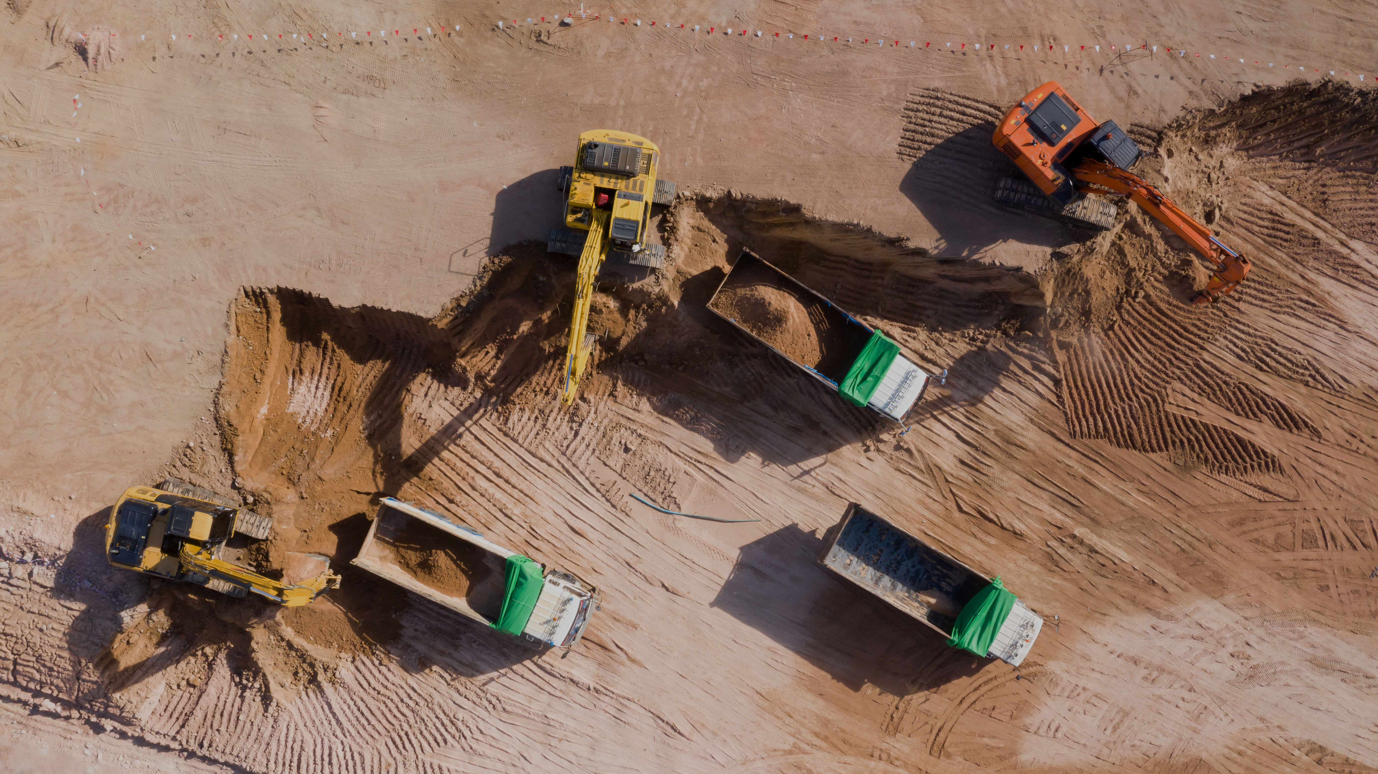 Aerial view of a construction site with excavators and dump trucks moving earth, illustrating large-scale civil works and construction products in use
