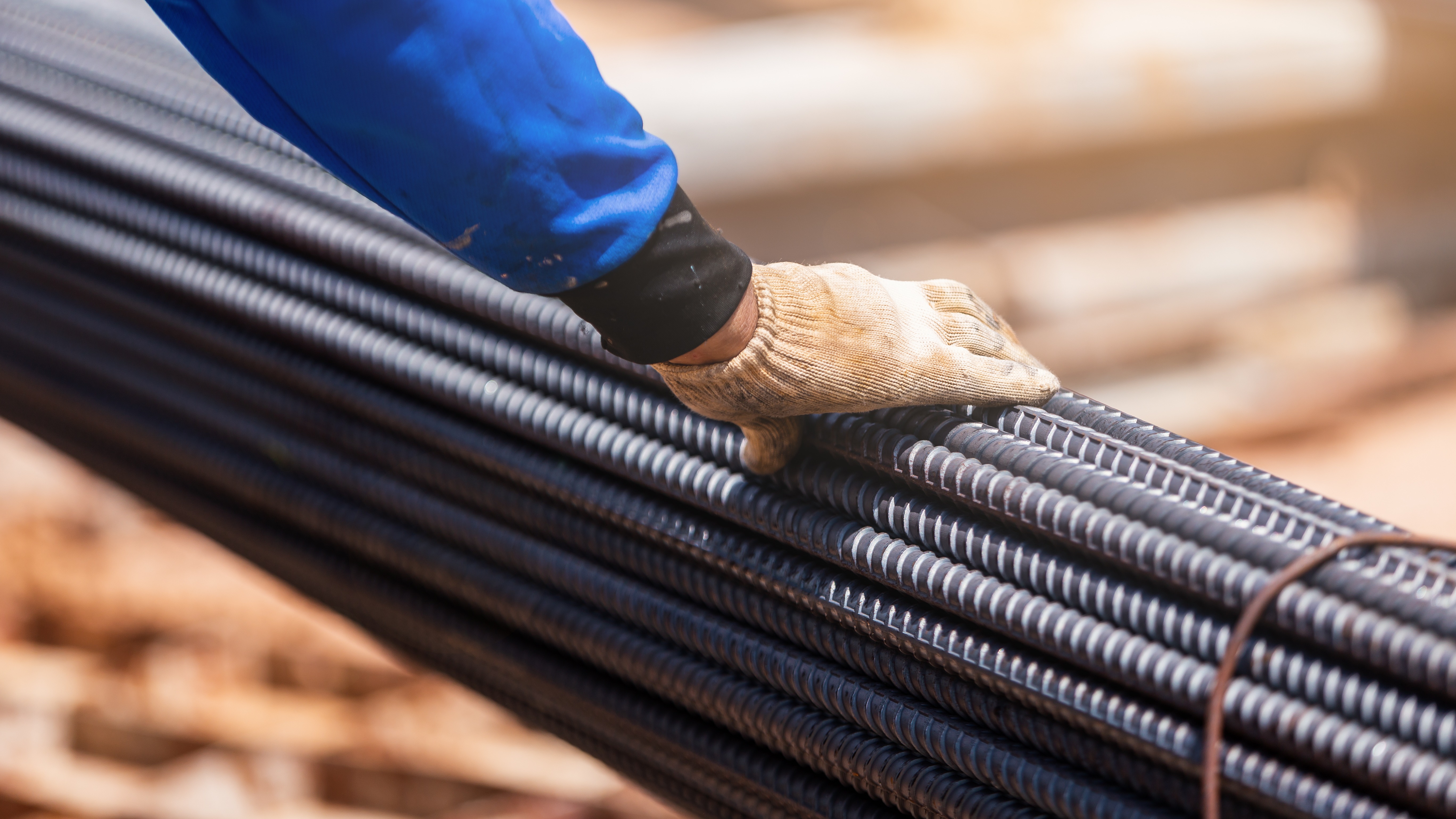 Construction worker wearing protective gloves stacking or aligning steel reinforcing bars on a construction site, illustrating structural construction products in use