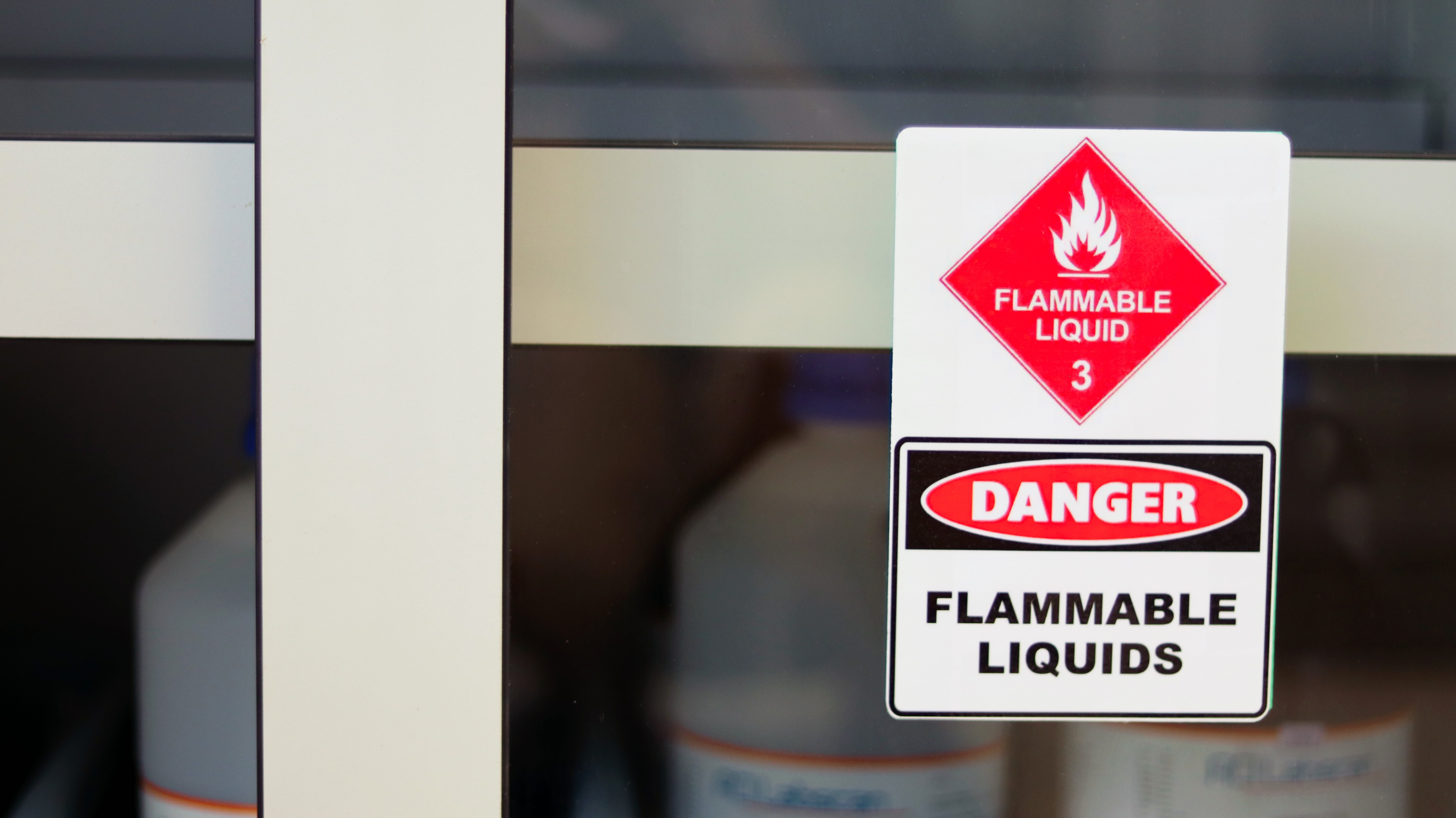 Close-up of a cabinet door with a red and white ‘Flammable liquid’ hazard sign, indicating explosive or flammable substances in a controlled industrial environment