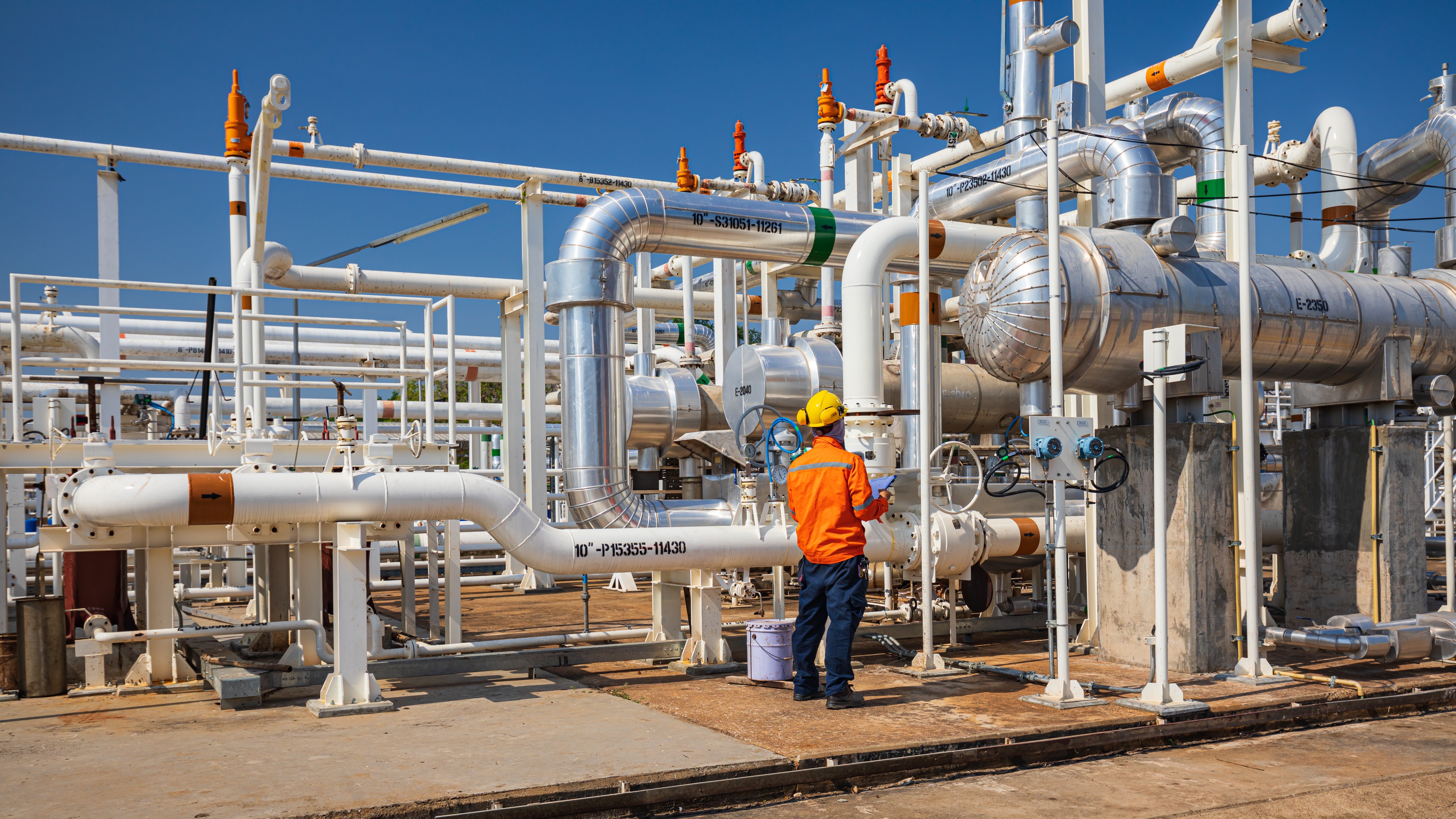 Engineer in protective clothing inspecting a network of stainless-steel pipes, vessels, and valves in an industrial plant, representing ASME pressure equipment