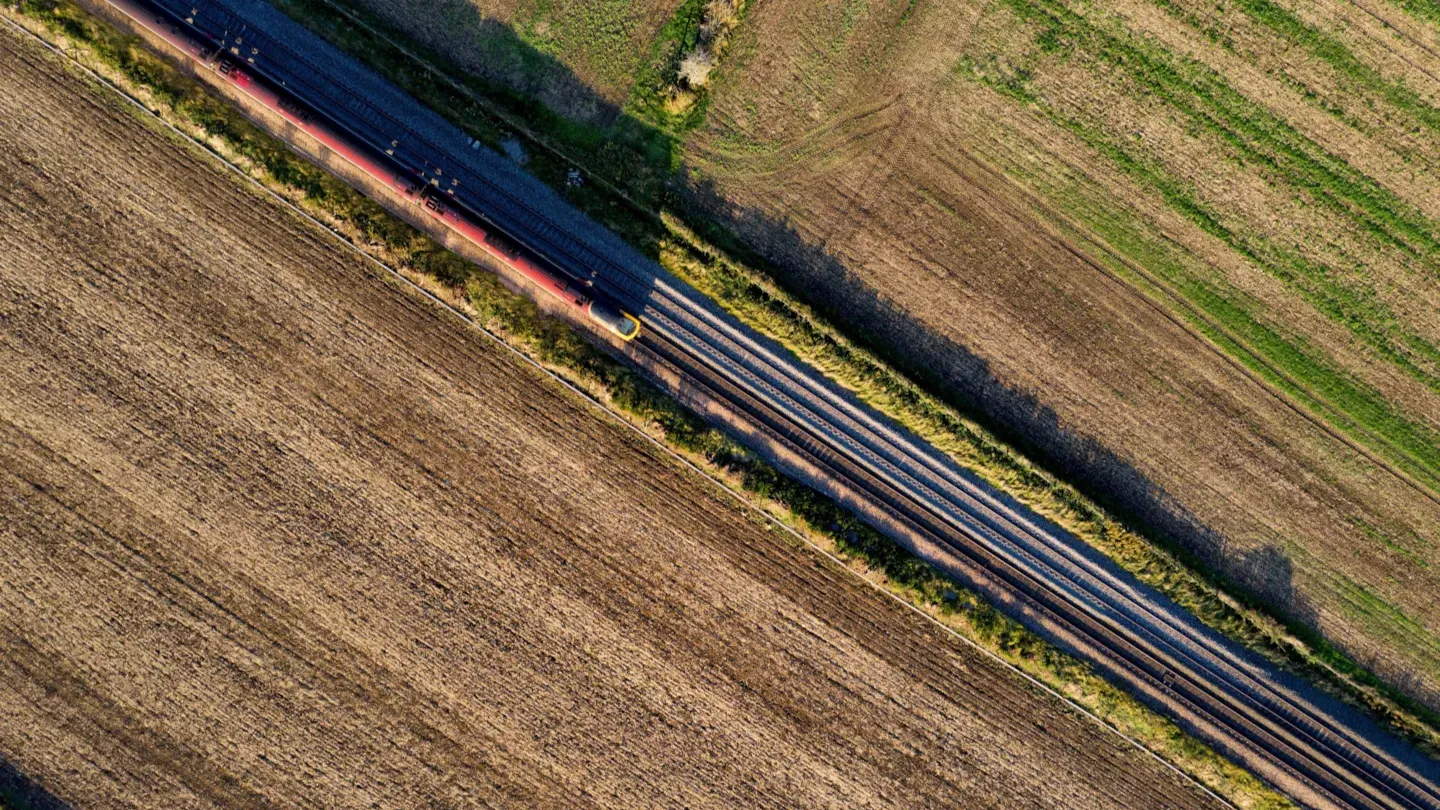 Aerial view of a freight train traveling through rural railway infrastructure, highlighting track condition and operational continuity