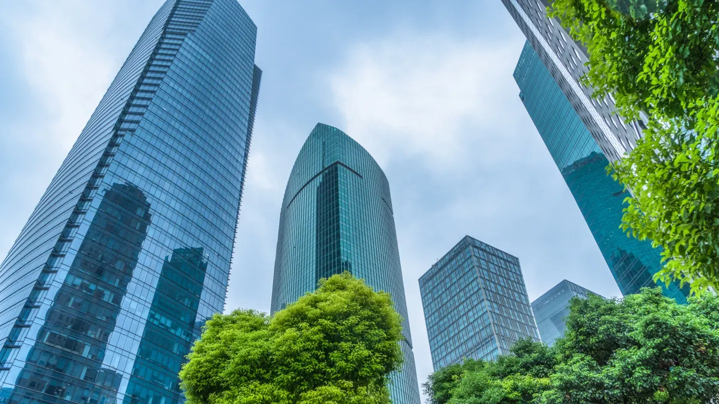 Modern glass skyscrapers surrounded by green trees, symbolizing credible climate finance and independent bond verification