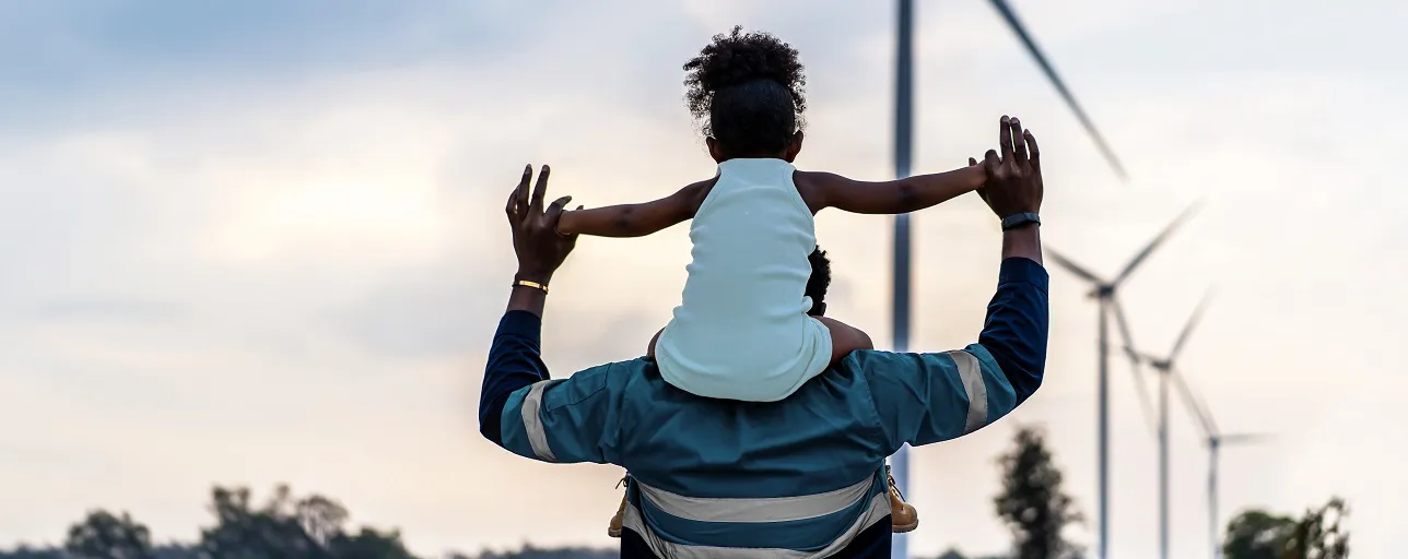 Black african father engineer holds his daughter in his arms at the wind turbines with great freedom. Concept of environmental engineering, renewable energy and love for nature and for the family