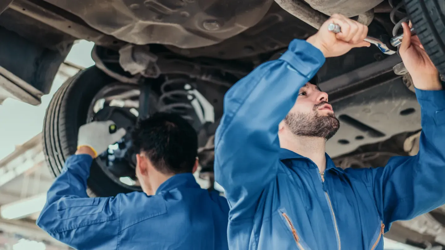 Automotive engineers inspecting a vehicle from underneath, representing system evaluation and safety validation