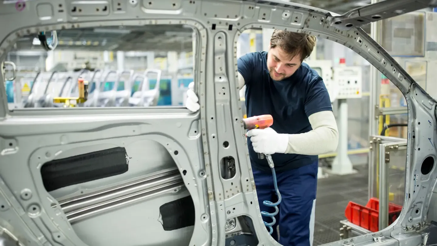 Automotive technician inspecting a vehicle body frame on the production line to support process improvement and compliance