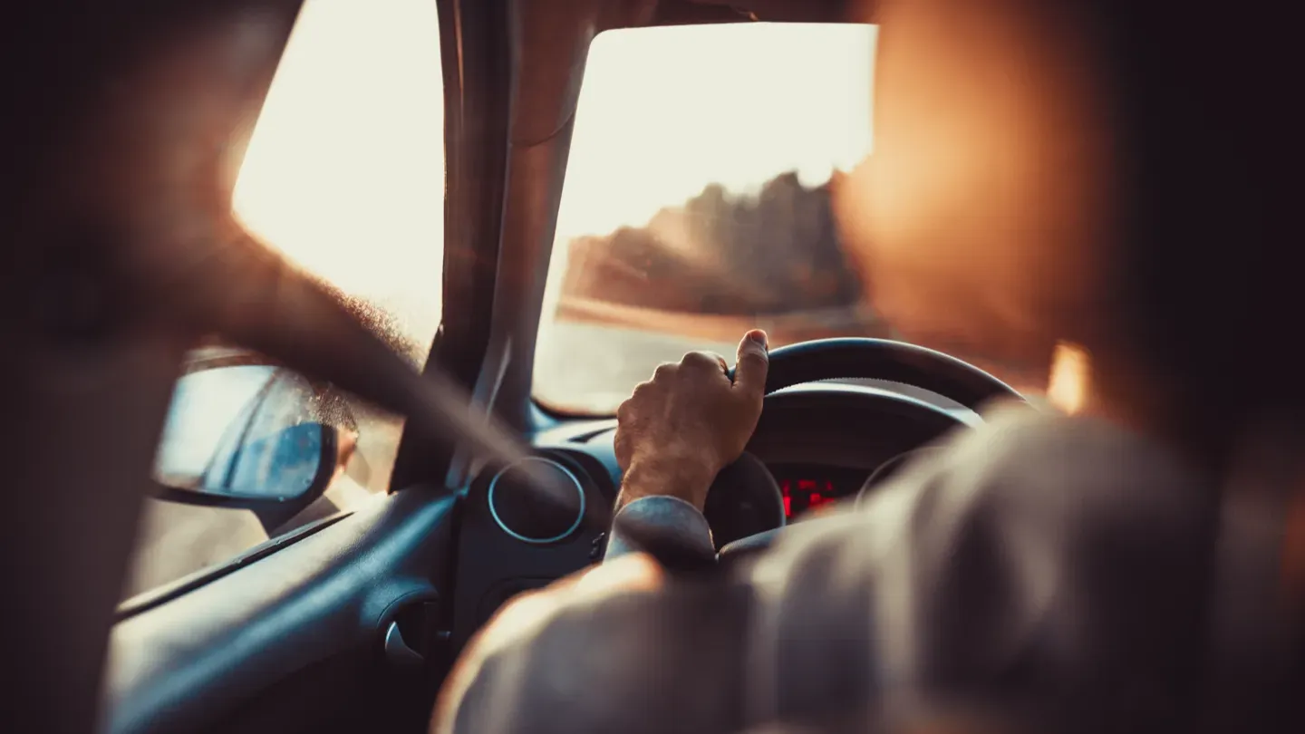 Driver holding the steering wheel at sunset, symbolizing performance insights and competitive positioning in automotive benchmarking
