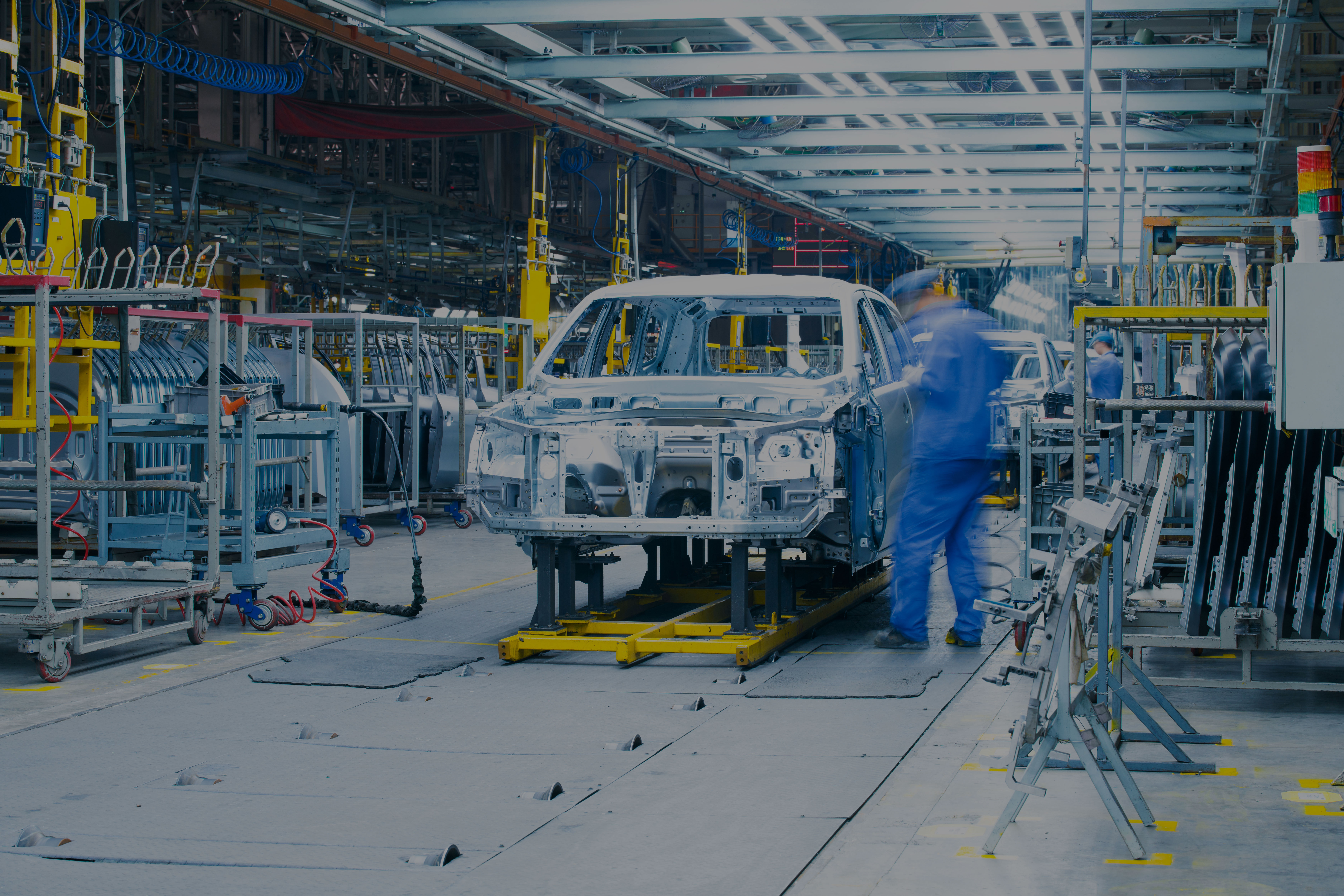 Automotive assembly line with an unfinished car body and technicians working under bright overhead lights, illustrating end-to-end process control and quality audits in vehicle manufacturing