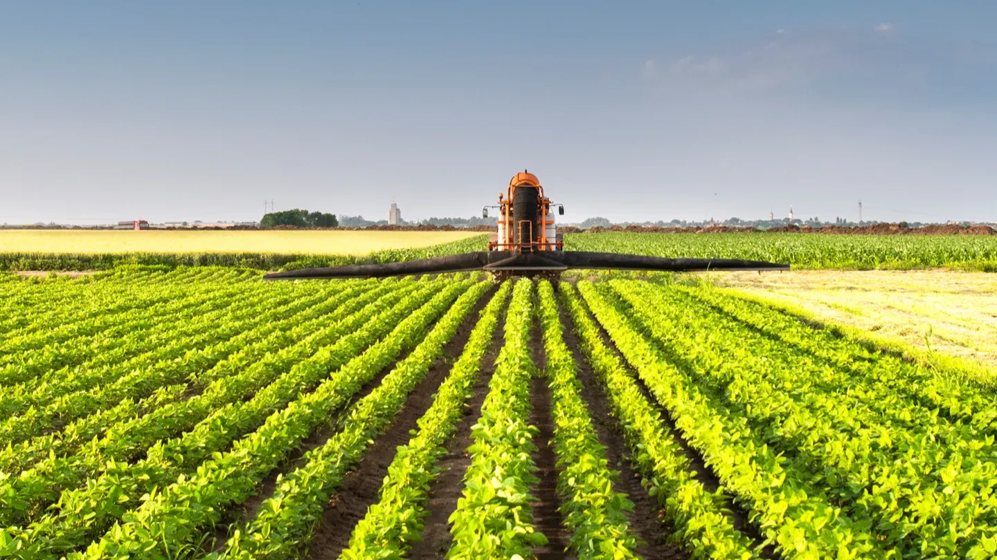 Tractor moving through rows of crops in a large field, illustrating sustainable farming practices and low-carbon agriculture