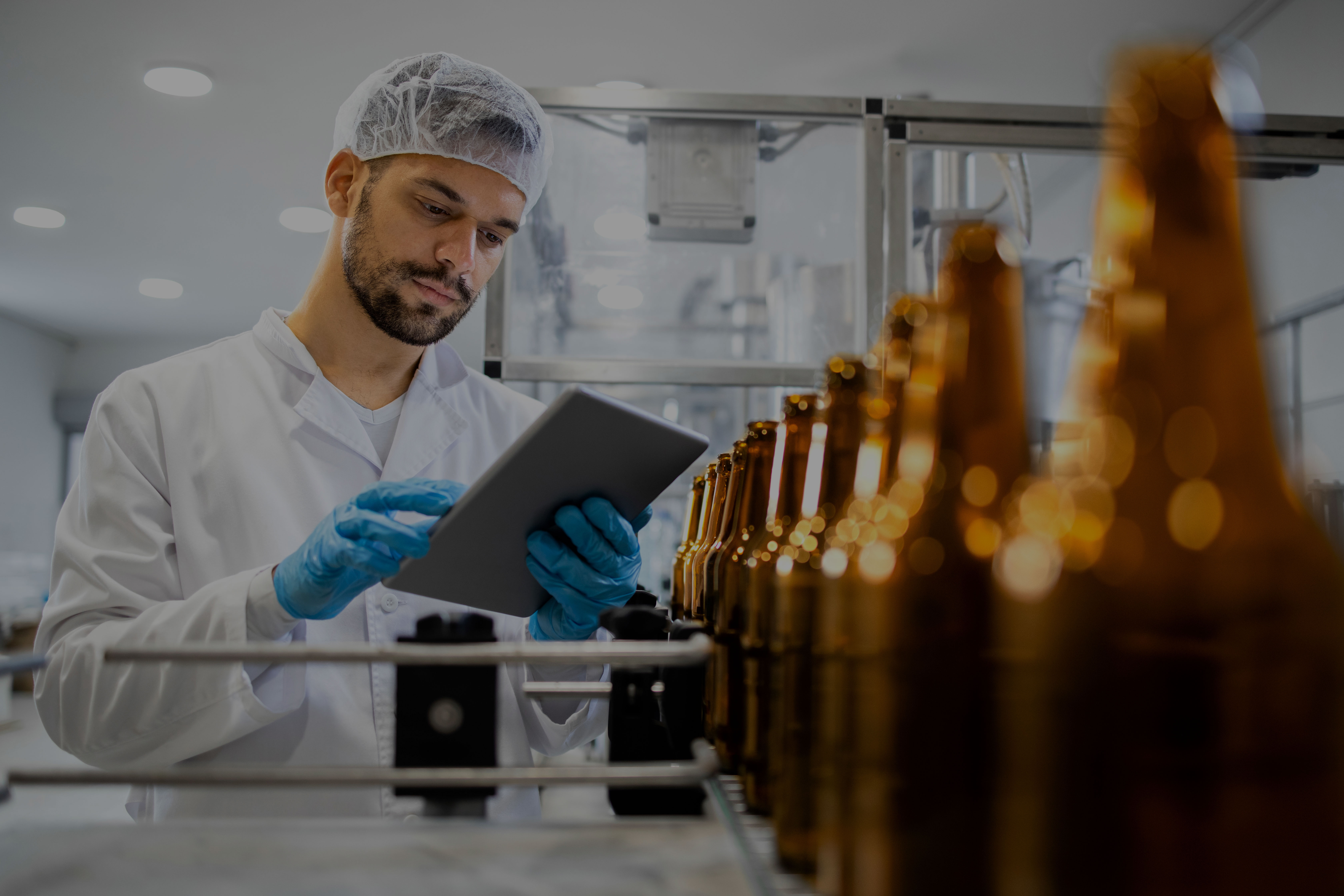 Food safety auditor in a white lab coat inspecting a production line of beverage bottles, representing DNV’s food and beverage audit and certification services