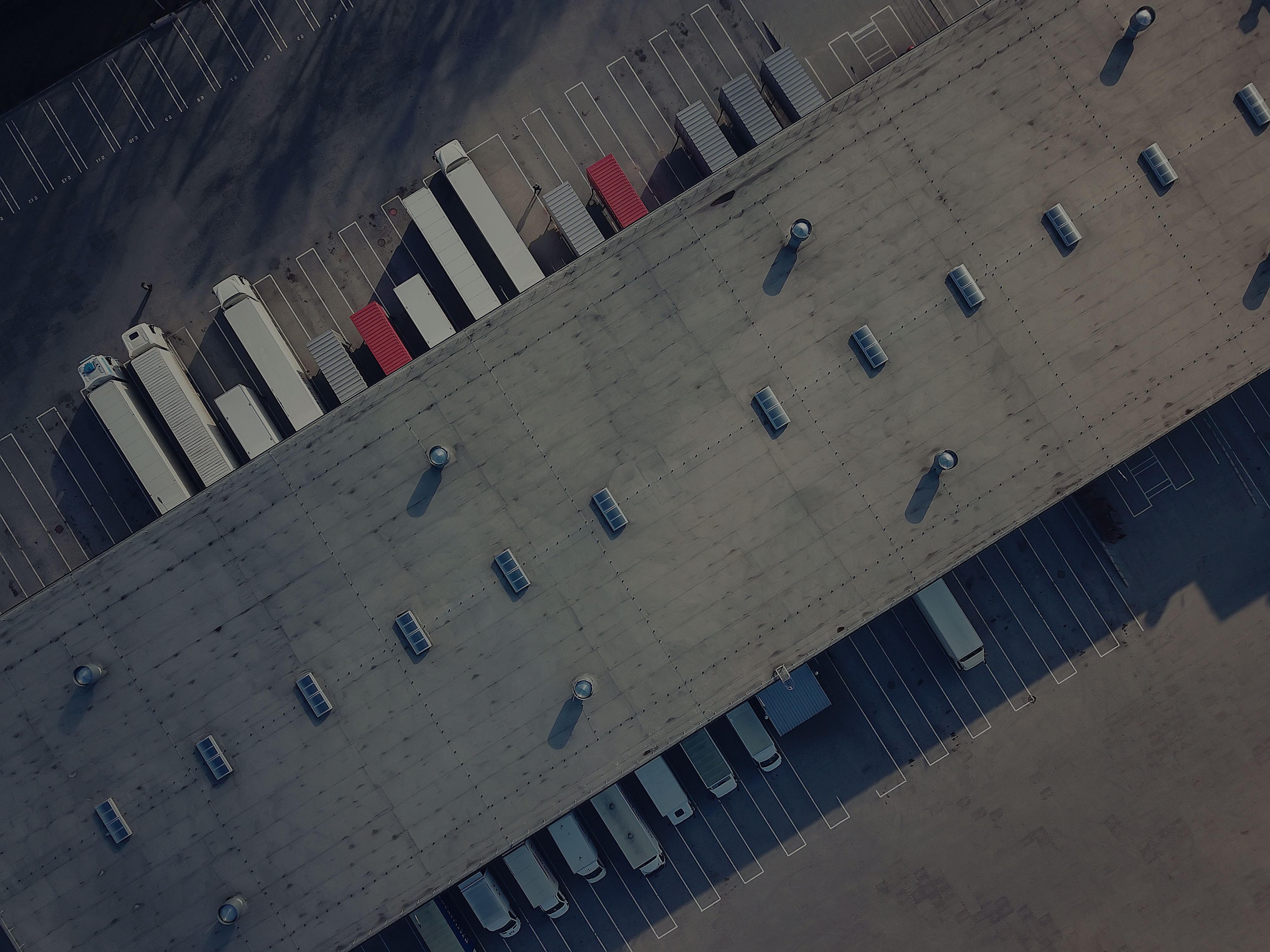 Aerial view of a modern logistics facility with delivery trucks and warehouse rooftop, symbolizing global supply chain management and operational resilience.