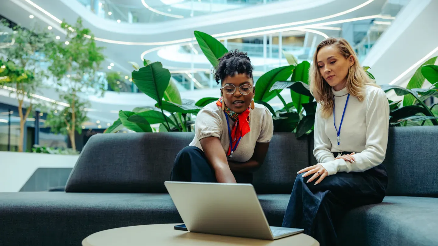 Two sustainability professionals reviewing climate and ESG data on a laptop in a modern office space, illustrating DNV’s support for climate, biodiversity, and decarbonization strategy development