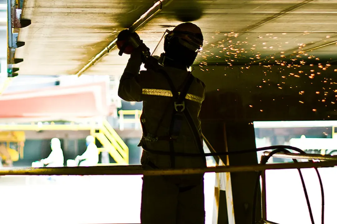 Welder in protective gear working on a steel structure in a manufacturing plant