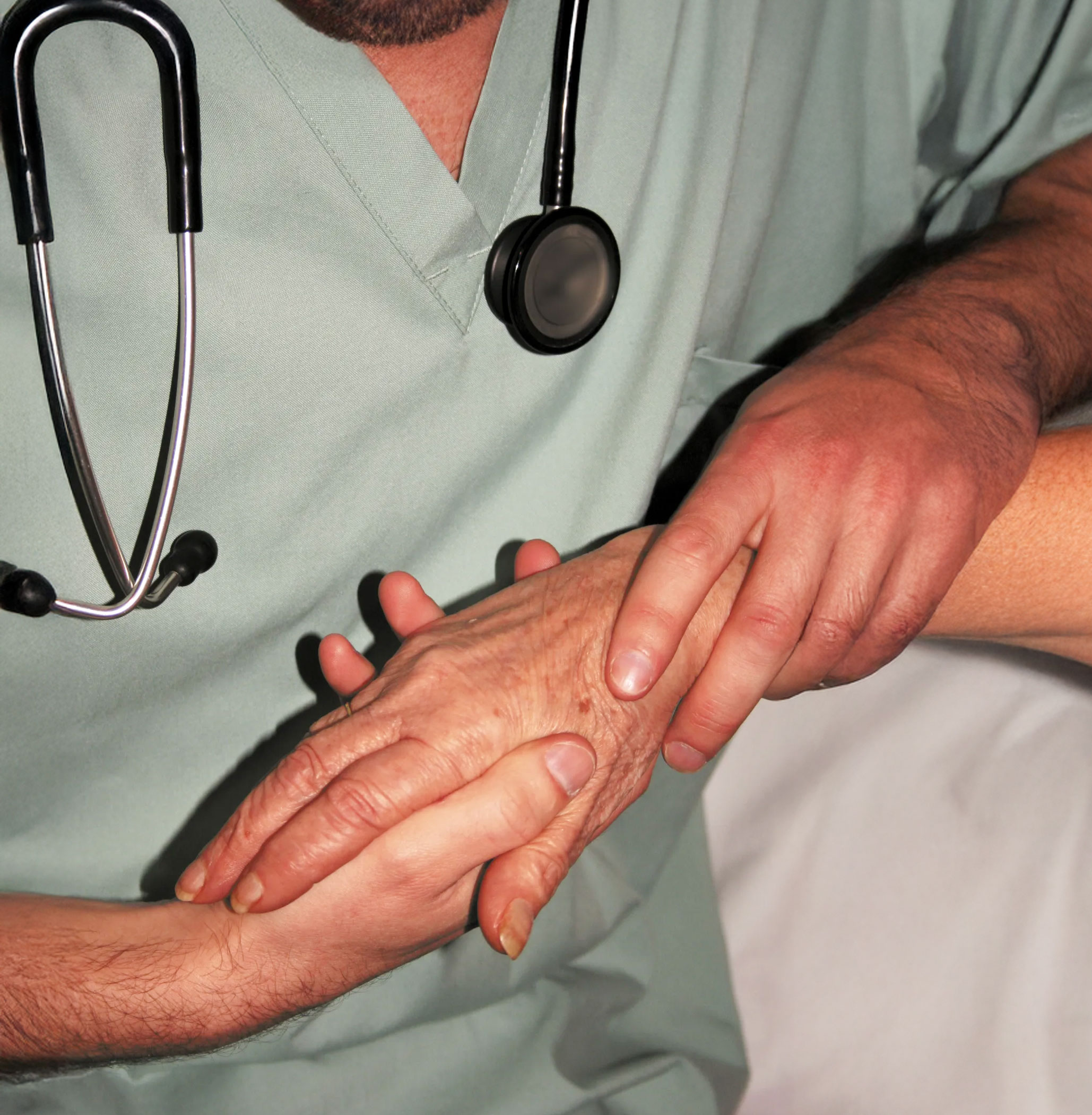 Doctor holding a patient’s hand with stethoscope visible, representing compassionate, evidence-based palliative care in DNV Advanced Palliative Care Certification programs