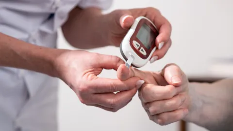 Healthcare professional using a glucometer to check a patient’s blood glucose levels, symbolizing safe, evidence-based glycaemic management in hospital care.