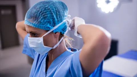 Healthcare professional adjusting protective mask in a clinical setting, symbolizing DNV’s commitment to infection prevention, safety, and quality in healthcare environments.