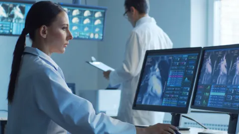 Medical professionals monitoring cardiovascular data on computer screens in a hospital control room, reviewing heart imaging and patient metrics related to ventricular assist device care.