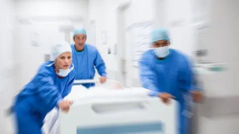 Medical team in surgical attire rushing a patient on a hospital gurney through a corridor, symbolizing rapid response and critical access hospital care.