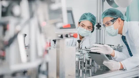 Two engineers wearing protective lab clothing inspect medical device components on a production line, symbolizing TCP III certification and regulatory compliance for medical devices in Taiwan.