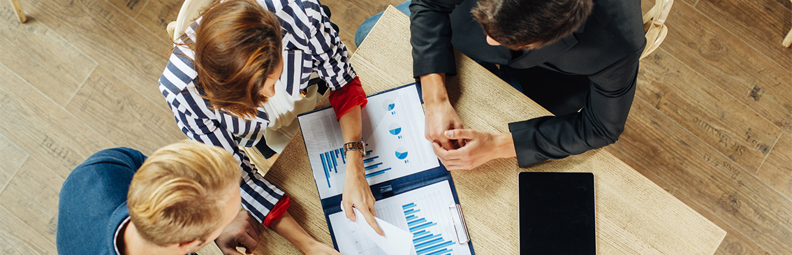 Liten grupp sitter runt ett bord och diskuterar dokument. Sett från ovan.